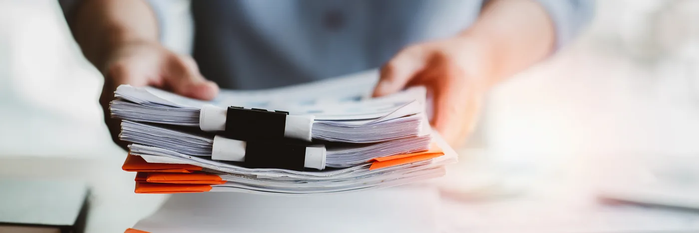 A pair of hands squaring up a thick stack of clipped paper documents on a desk.